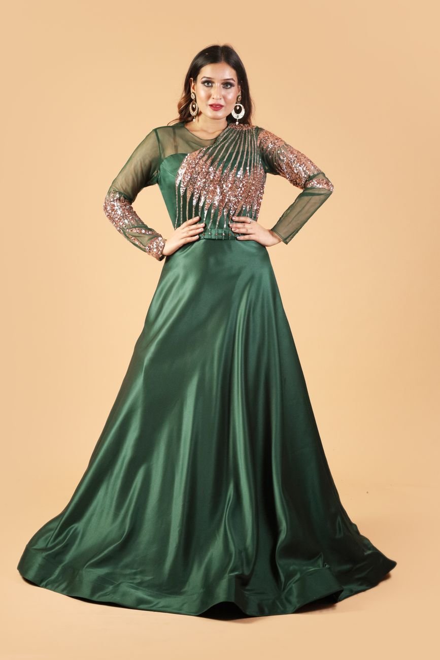 Woman in a green satin evening gown posing against a beige background.