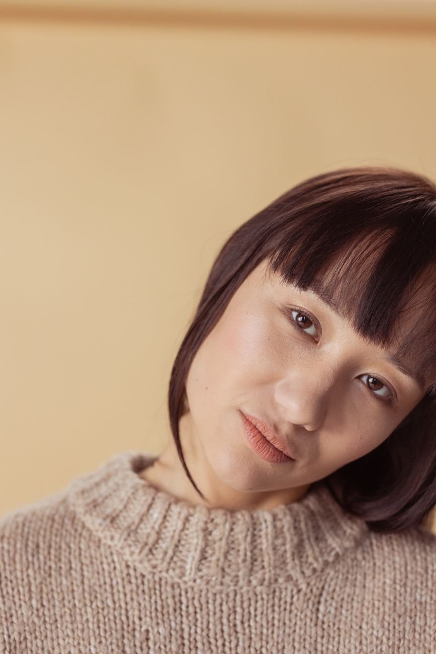 Studio portrait of a woman in a knitted sweater with a neutral beige background.