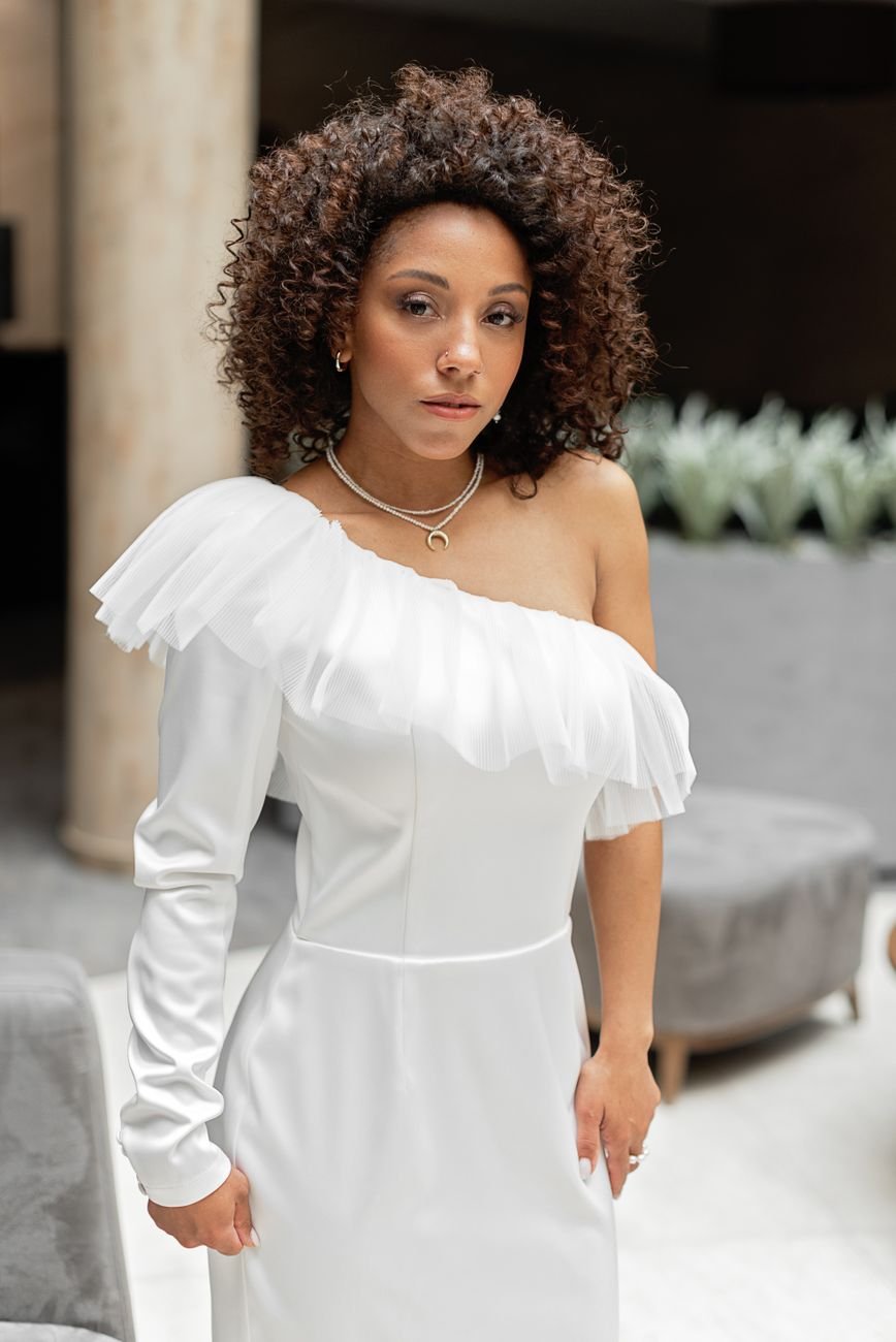 Woman in a modern one-shoulder white dress with natural curly hair.
